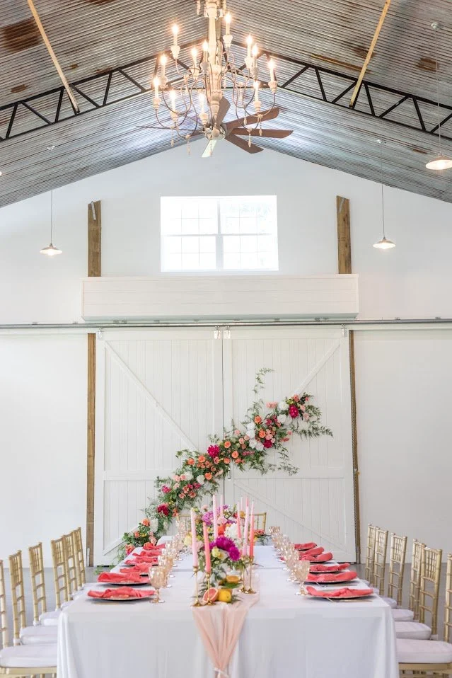 A chandelier above a dressed reception table inside the barn