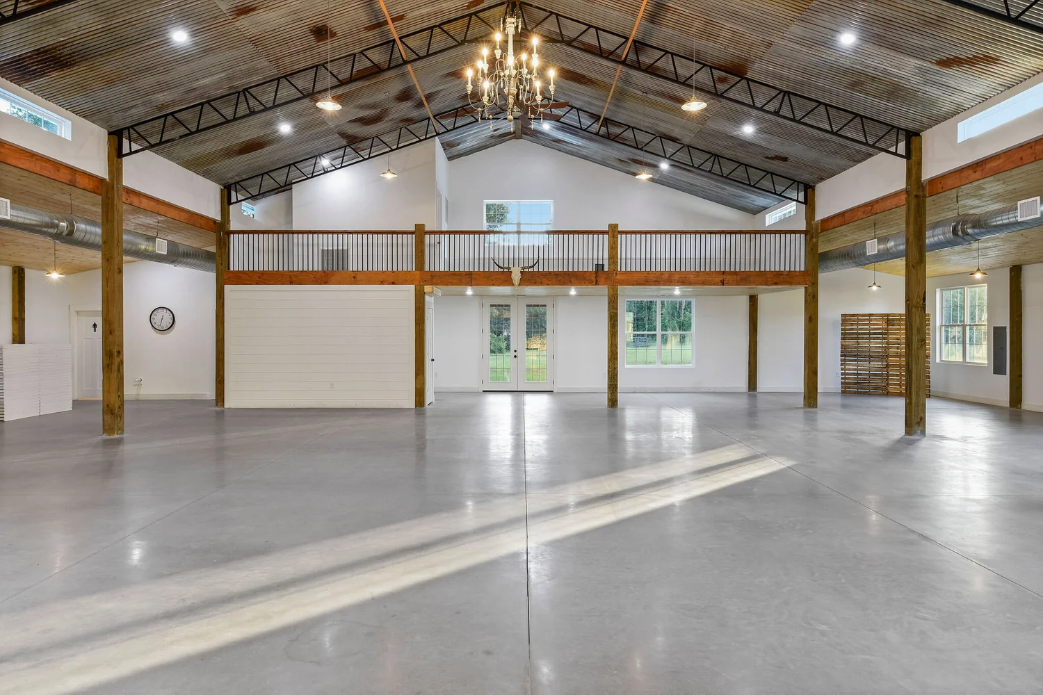 The empty barn interior: white walls, exposed beams, a chandelier and a polished concrete floor