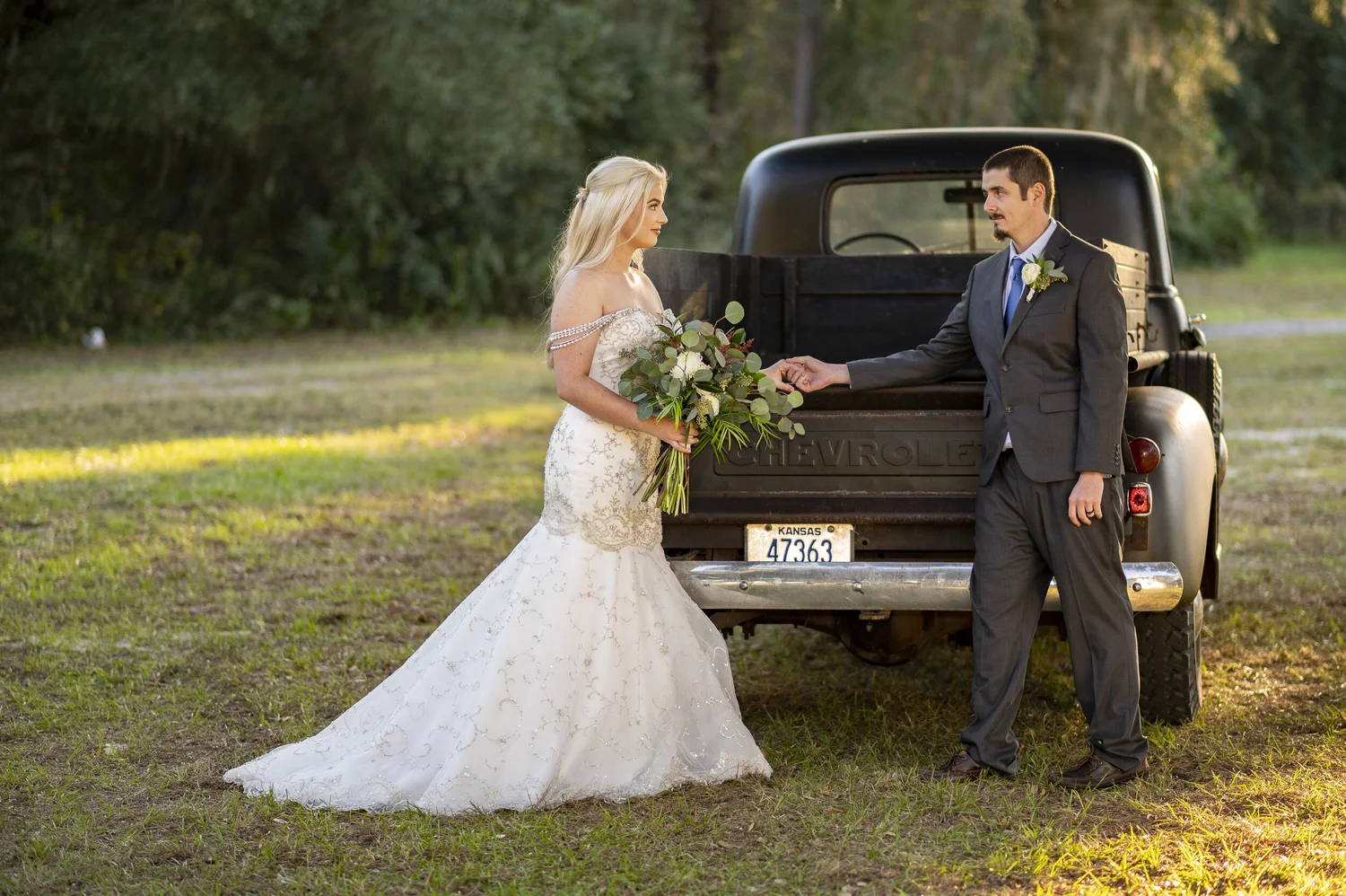 A bride handing her bouquet to the groom beside a vintage black pickup truck