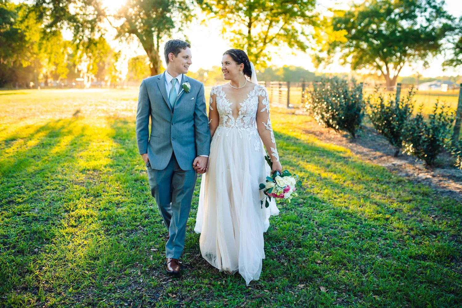 A bride and groom walking hand in hand across the grounds in golden light