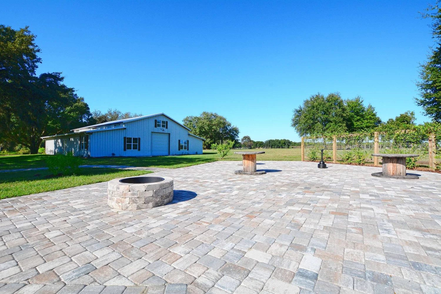 A paver patio with a fire pit and seating, the barn in the distance under a blue sky