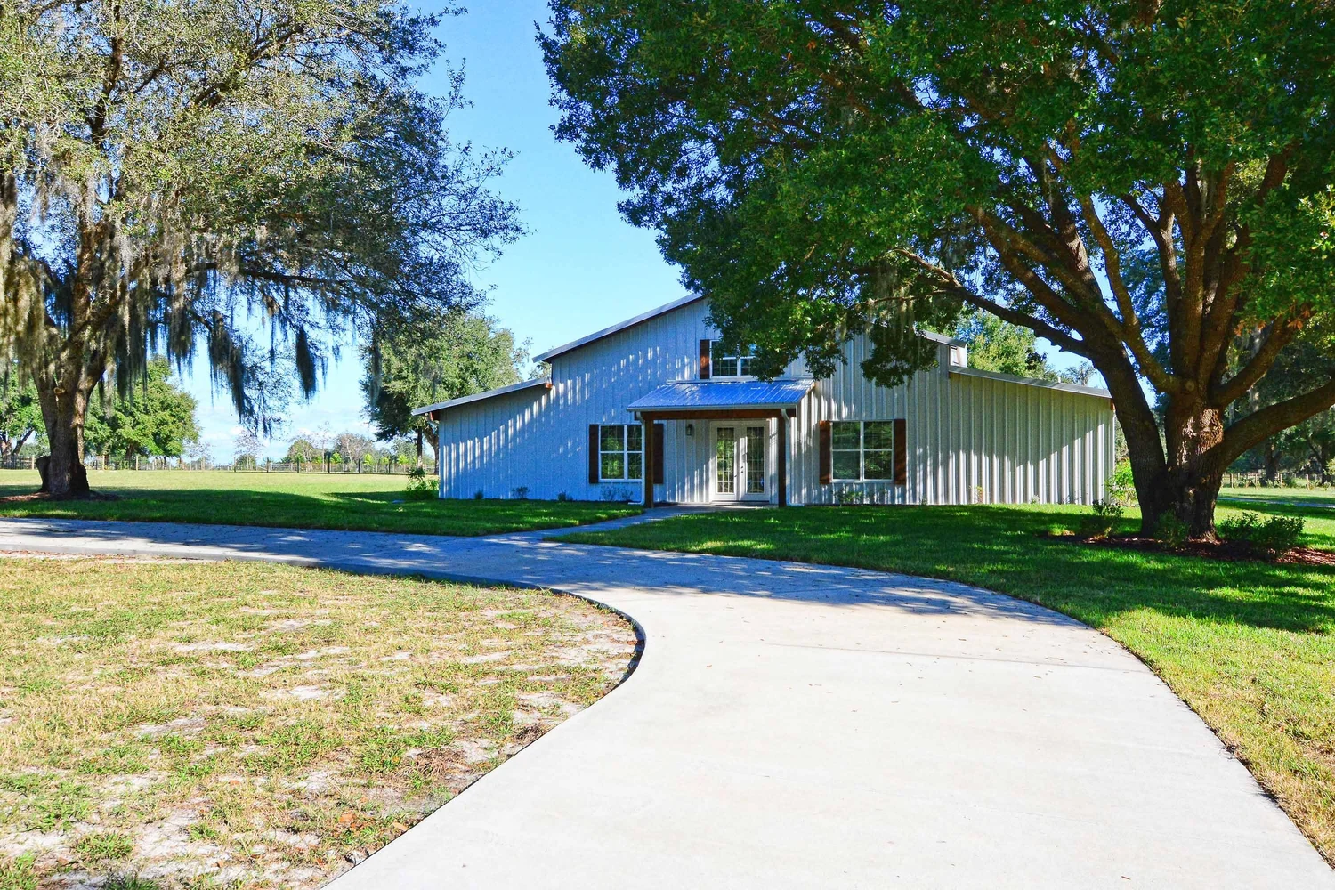 The white barn at Southern Oaks under spreading live oaks, with a curving path across the lawn